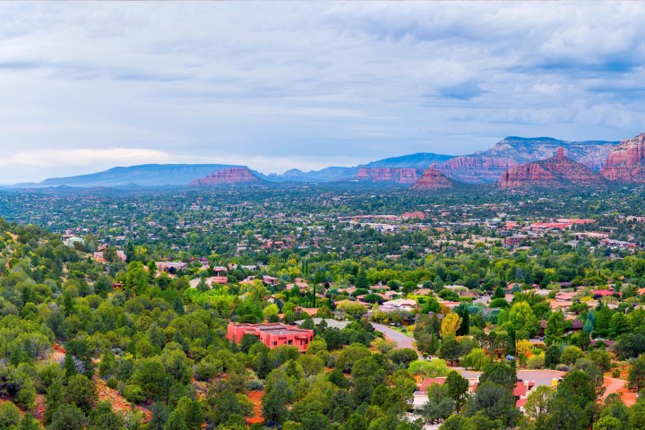 Panoramic view of Sedona, Arizona with red rocks, green trees, and a winding road.