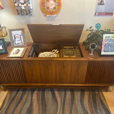 Vintage wooden record player console with framed art and potted plant on top.