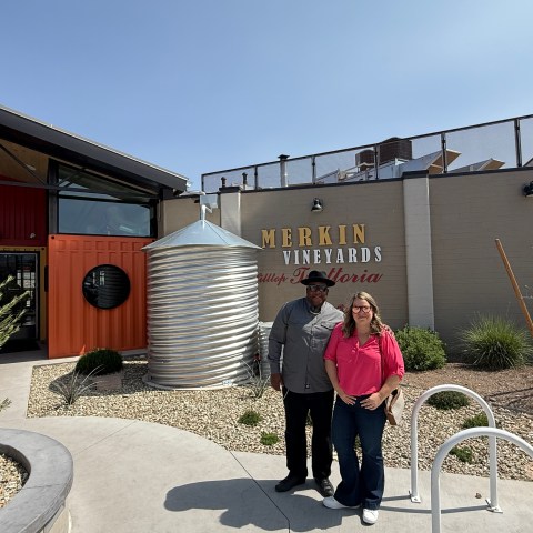 Two people standing outside Merkin Vineyards building on a sunny day.