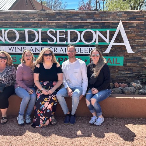Five people sitting in front of Vino di Sedona sign on a sunny day.