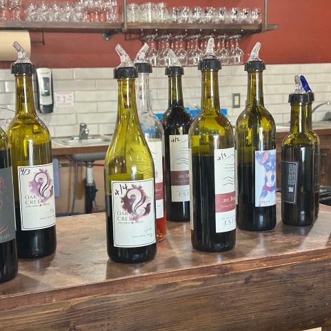Eight wine bottles with various labels on a wooden bar counter.