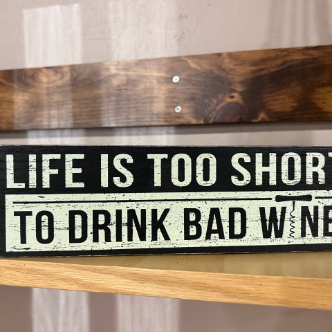 Sign reads: 'Life is too short to drink bad wine' on a wooden shelf.