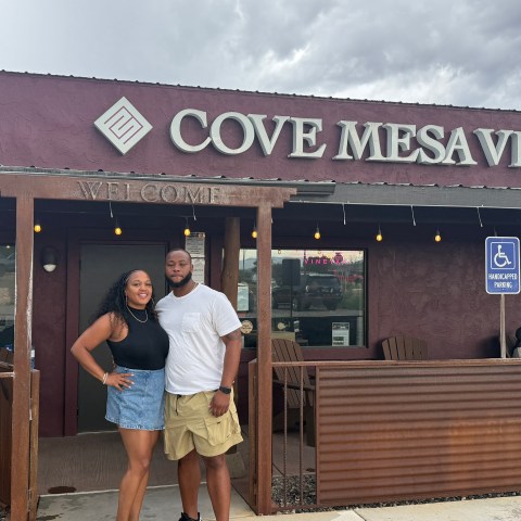 Two people posing outside Cove Mesa Vineyard under cloudy sky.