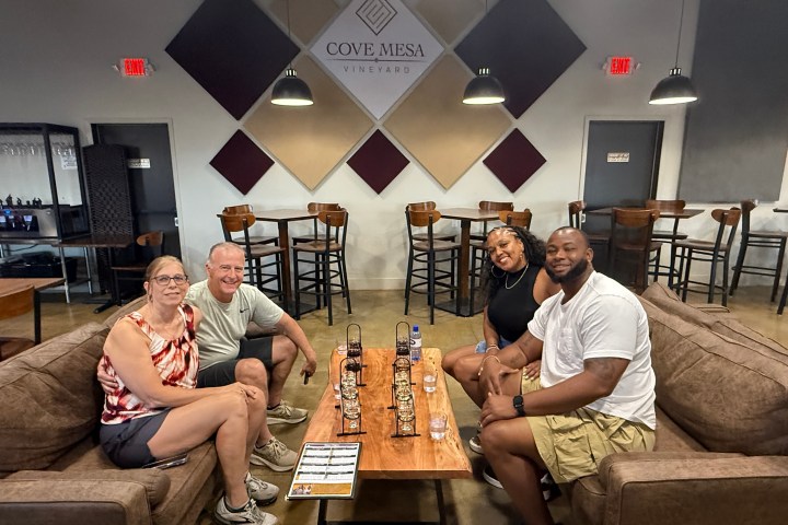 Two couples seated at a table in a tasting room with 'Cove Mesa Vineyard' sign.