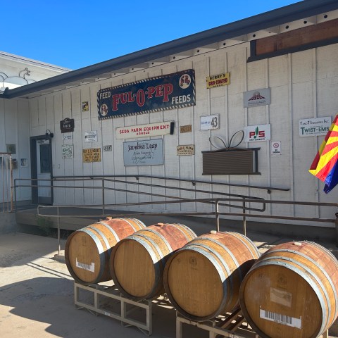 Three barrels on a rack in front of a building with vintage signs and Arizona flag.