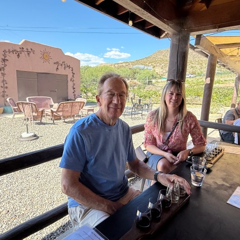 People sitting at an outdoor table with drinks, rustic setting and hills in the background.