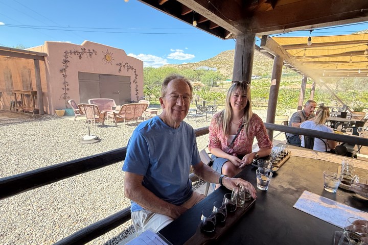 People sitting at an outdoor table with drinks, rustic setting and hills in the background.