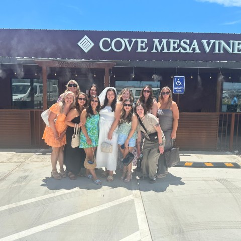 Group of women posing outside Cove Mesa Vineyard under a clear blue sky.