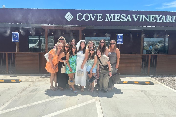Group of women posing outside Cove Mesa Vineyard under a clear blue sky.