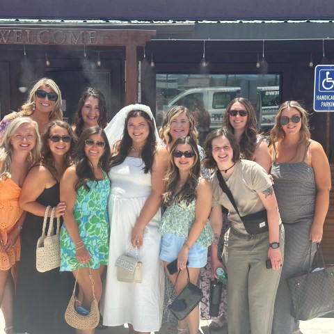 Group of women smiling outside a building under a 'Welcome' sign.