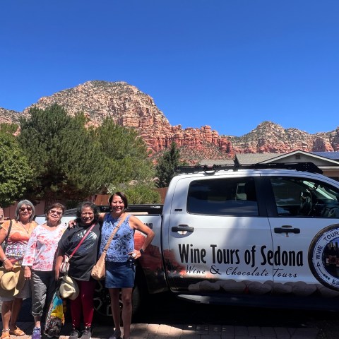 Four women standing by a 'Wine Tours of Sedona' van, with red rock formations in the background.