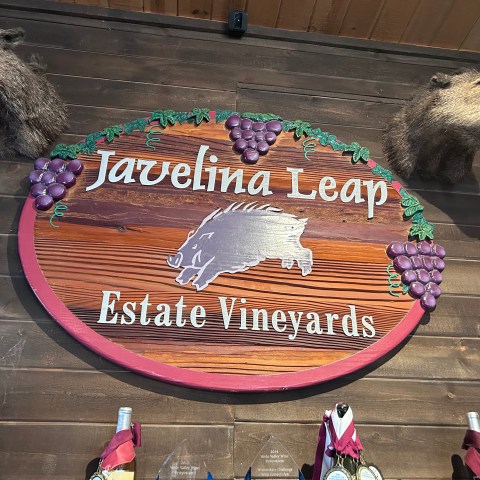 Sign reading 'Javelina Leap Estate Vineyards' with javelina heads and grape decorations on a wooden wall.