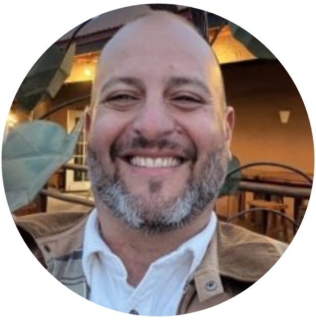 Smiling man with a beard outdoors, wearing a jacket.